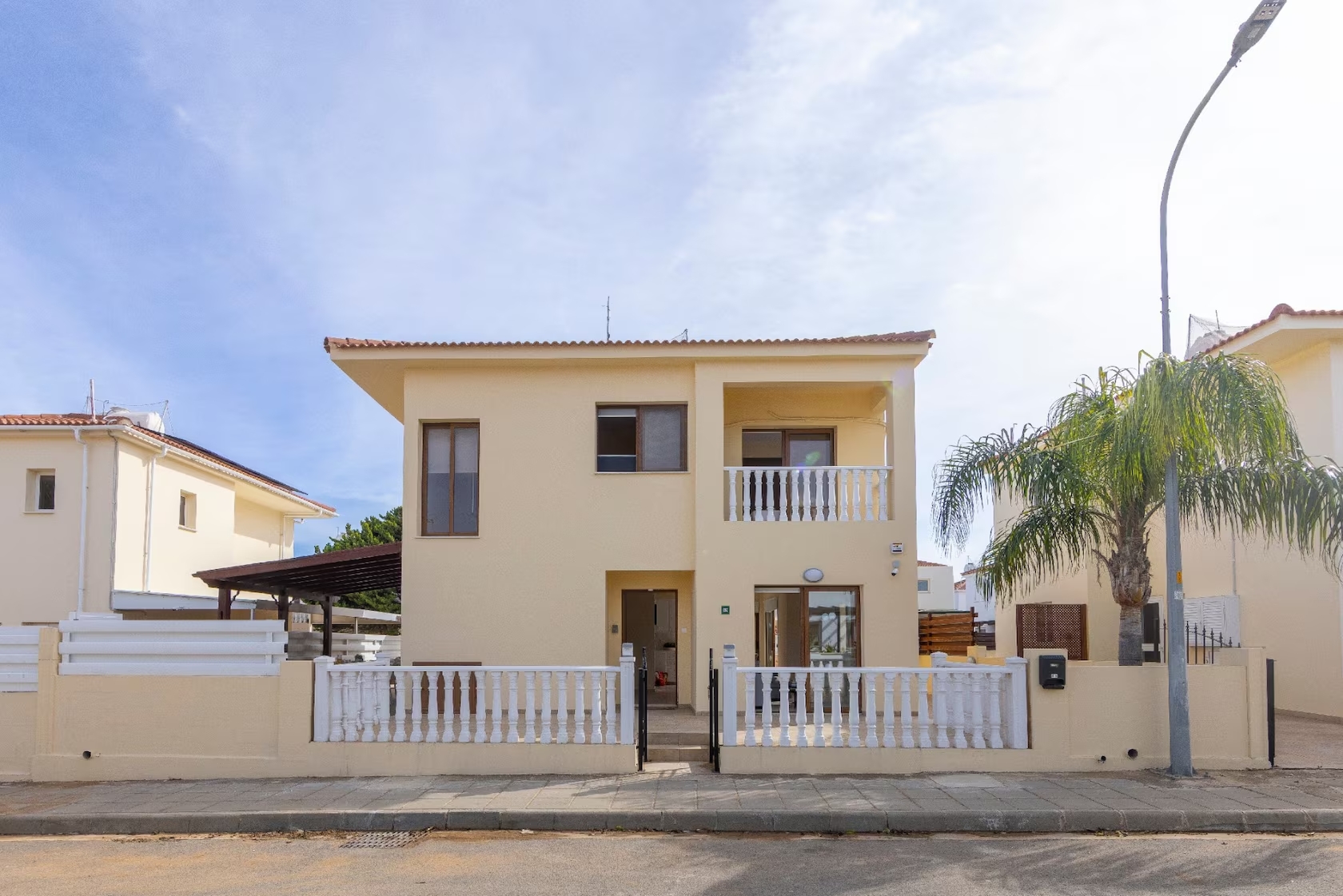 Front facade of Villa Poseidon with an upstairs balcony, white balustrades and a palm tree
