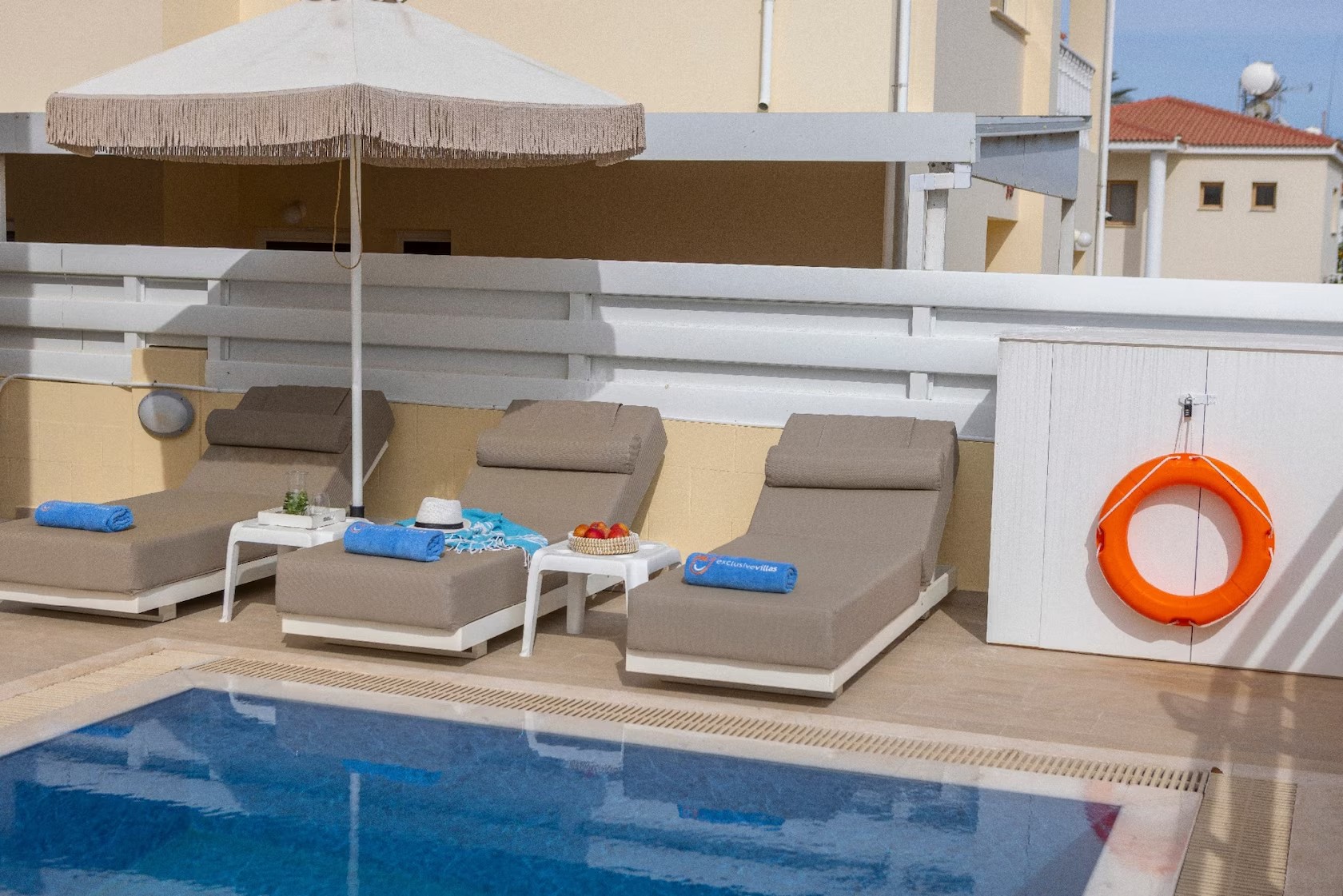 Three sunbeds with blue towels and a parasol beside the swimming pool