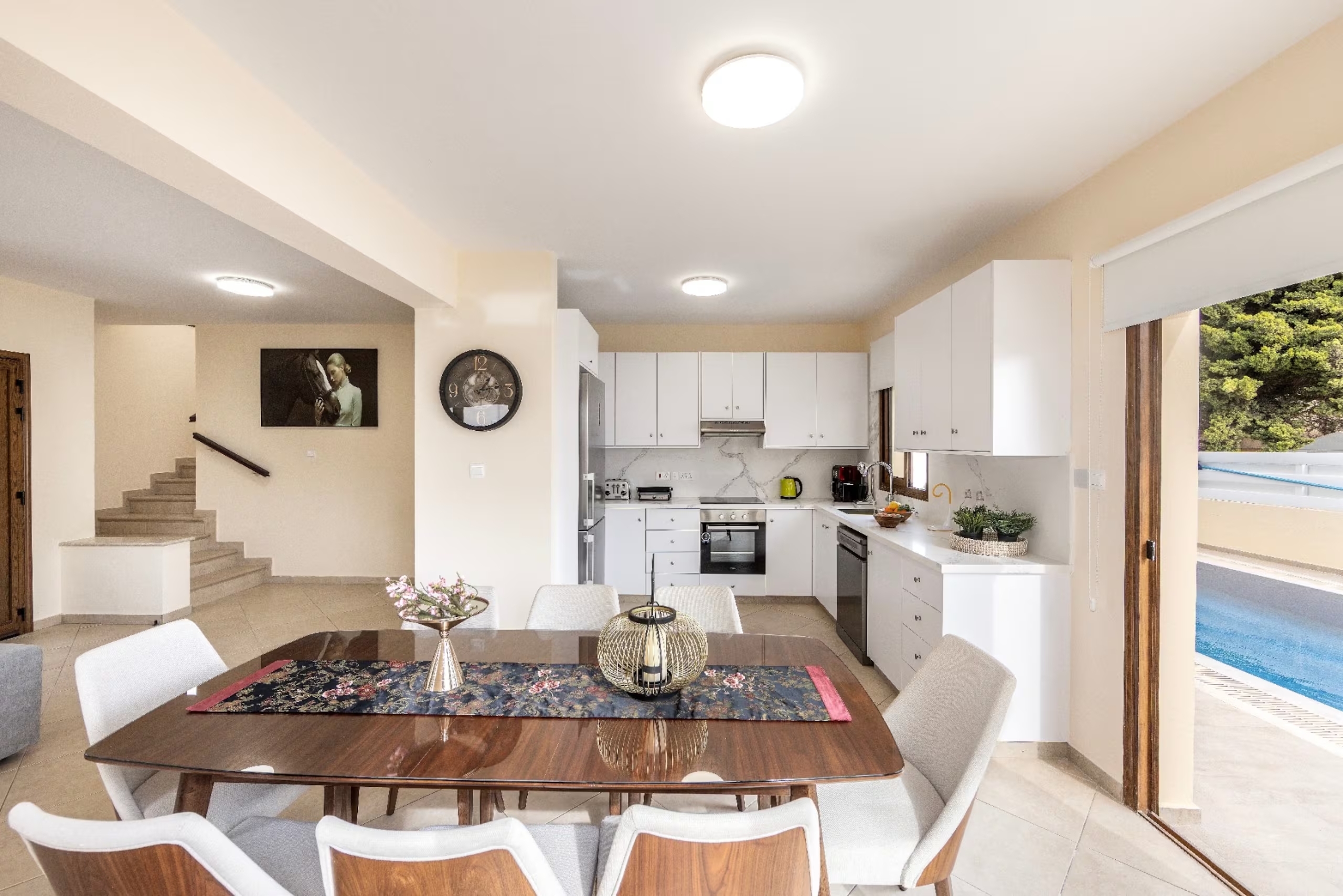 Dining table and open-plan kitchen with swimming pool visible through the sliding doors