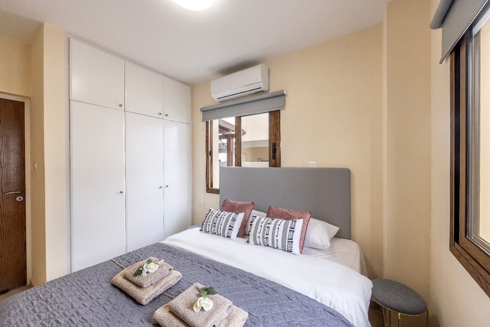 Double bed with grey bedding beside a white fitted wardrobe