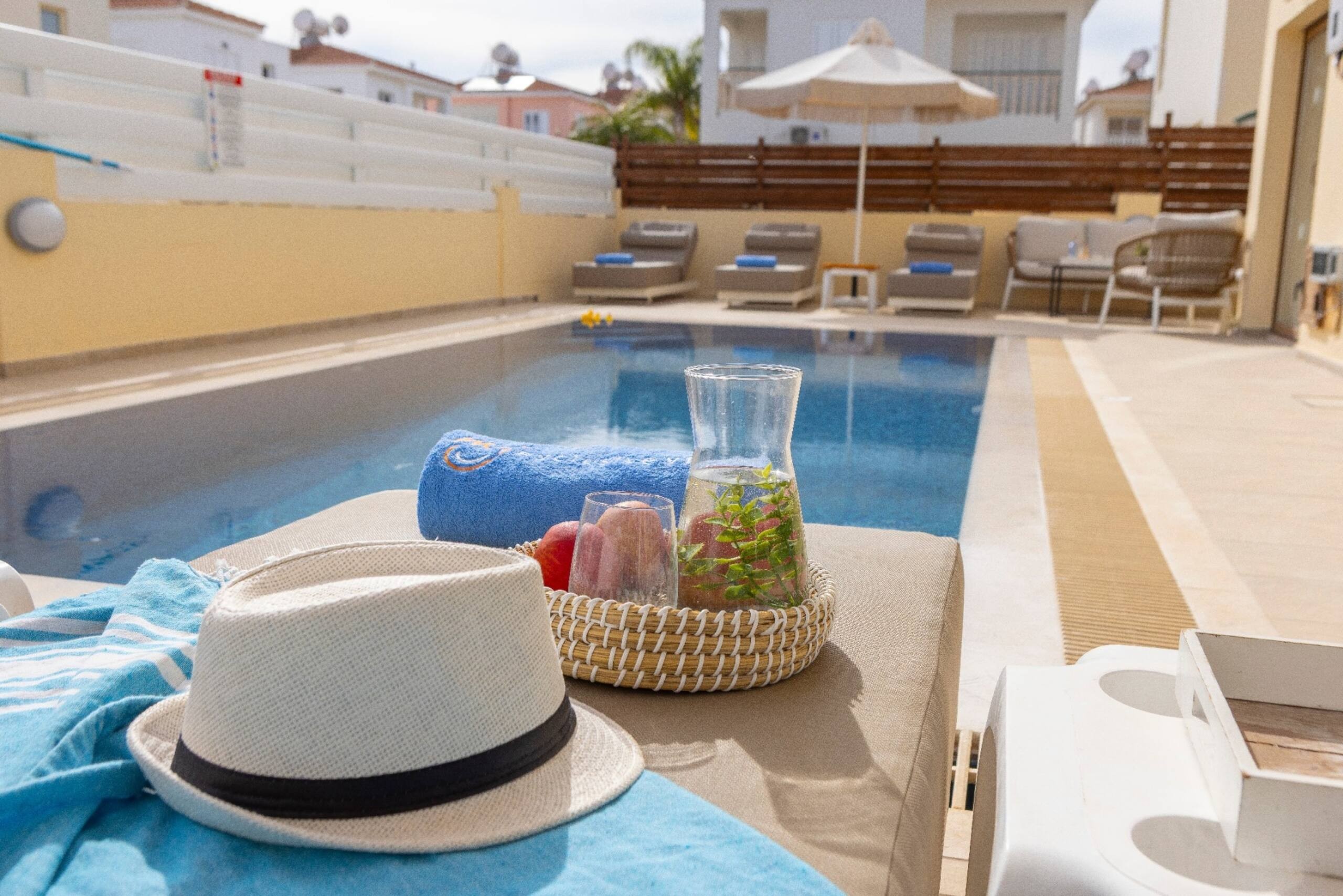 Hat, blue towel and drinks on a sunbed overlooking the swimming pool