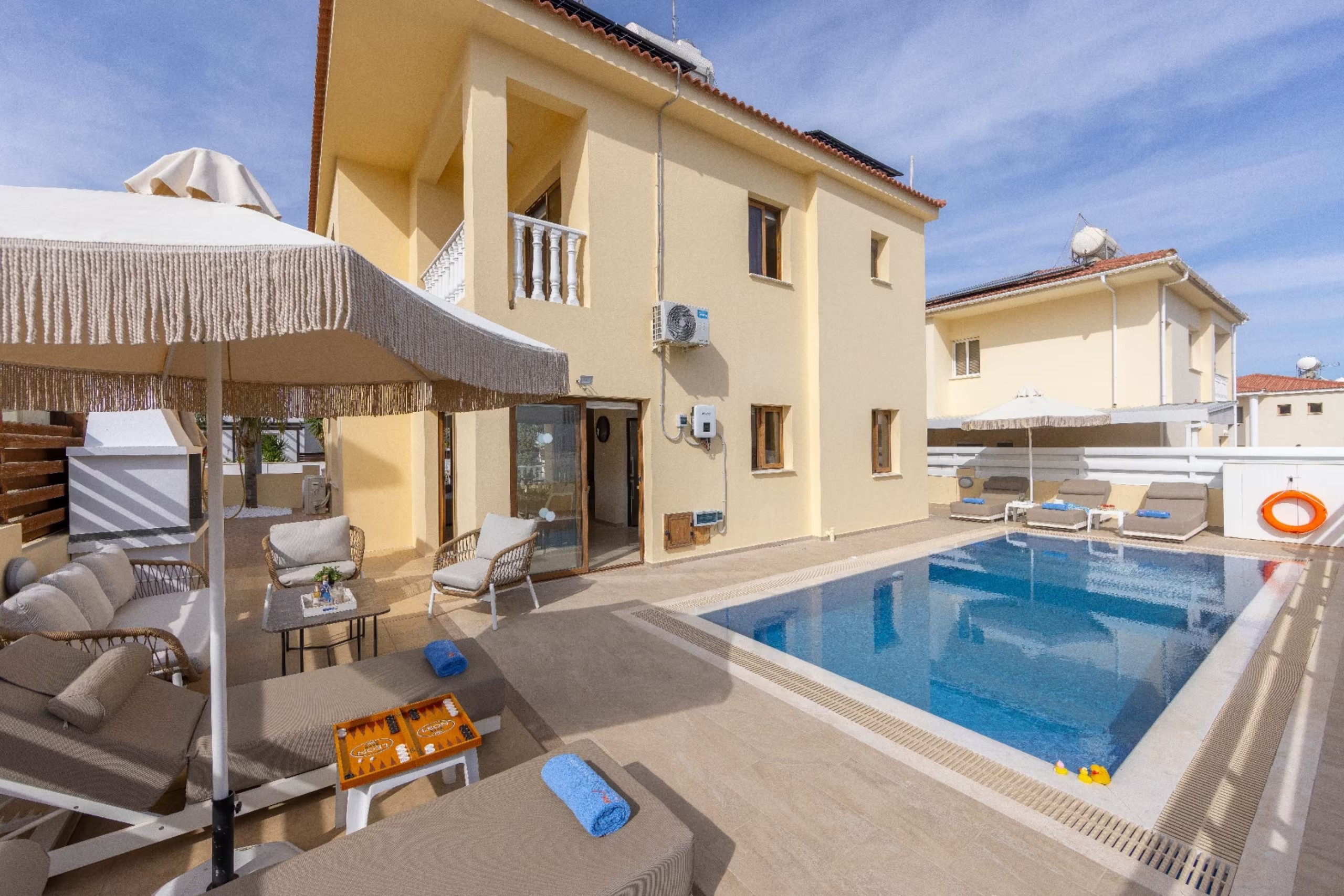 Villa Poseidon seen from its swimming pool with shaded seating and sunbeds