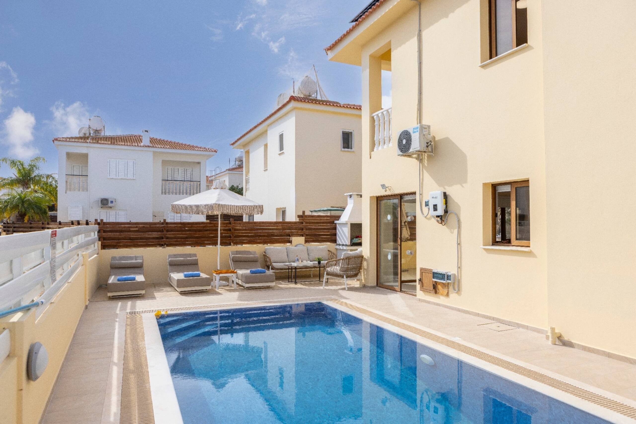 Swimming pool alongside Villa Poseidon with sunbeds, parasol and barbecue at the far end
